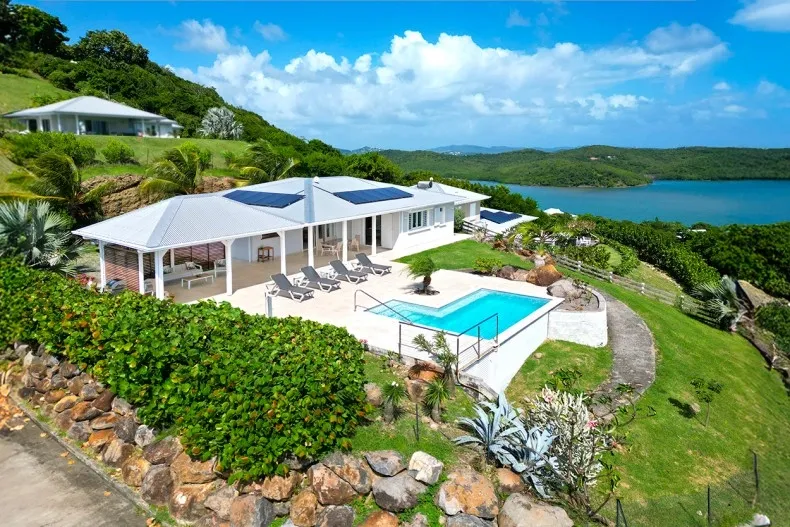 Luxury villa in Martinique with a pool overlooking lush hills and turquoise bay under a bright blue sky.