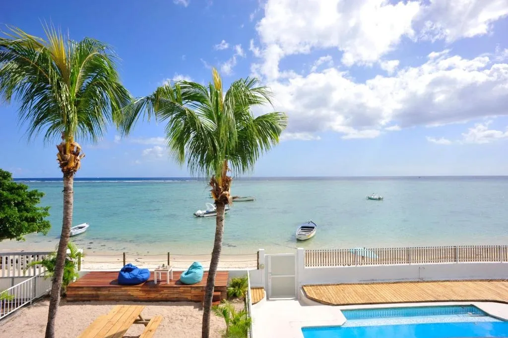 View of La Preneuse beach in Mauritius with palm trees, boats on turquoise water, and a villa pool area