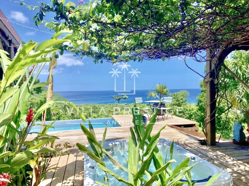 Luxury villa terrace with jacuzzi, tropical plants, and ocean view under a shaded pergola in Guadeloupe